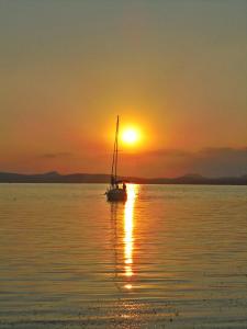 een zeilboot in het water bij zonsondergang bij Villa-Negra Retro Panzió in Balatonföldvár