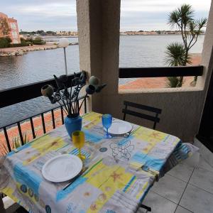 un tavolo con piatti e bicchieri e una vista sull'acqua di bel Appartement vue sur le lac marin avec WIFI et piscine a Le Barcarès