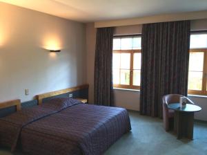 a hotel room with a bed and a table and windows at Hotel ABBEY in Grimbergen