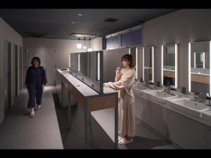 a woman standing in a public bathroom with sinks at Capsule Plus Yokohama Sauna & Capsule in Yokohama