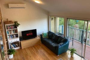 een woonkamer met een zwarte leren bank en een tv bij Kookaburra Retreat in Nelson Bay