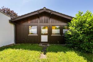 una casa marrone con una porta e un cespuglio di Ferienwohnpark Immenstaad am Bodensee Satteldachhaus Typ 9 SD 25 a Immenstaad am Bodensee