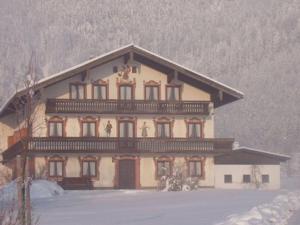 un gran edificio con nieve en el suelo delante de él en Schusterbauer-Hof, en Schleching