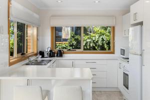 a white kitchen with white appliances and two windows at Reflections on the Bay in Hobart