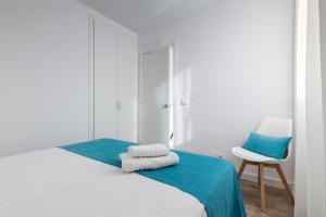 ein weißes Schlafzimmer mit einem Bett und einem Stuhl in der Unterkunft Apartamentos Playa Canutells in Maó