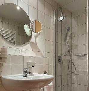 uma casa de banho com um lavatório e um chuveiro com um espelho. em Hotel Bettina garni em Günzburg