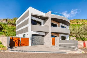 una casa blanca con puertas naranjas en una colina en Villa Belmonte by LovelyStay, en Ponta do Sol