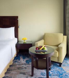 كراون بلازا جدة في جدة: غرفة في الفندق بها كرسي وطاولة مع وعاء من الفواكه