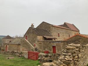 un antiguo edificio de piedra con puertas rojas y una pared de piedra en Le jardin de THELEME "Charme discret pour un nid douillet", en Mazille