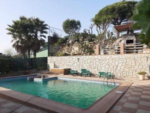 una piscina con sillas verdes y una pared de piedra en Habitaciones en Villa Coliving Casa Rural, en Sant Fost de Campsentelles