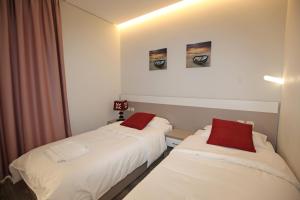 2 camas en una habitación con sábanas blancas y almohadas rojas en Star Hotel Saranda, en Sarandë