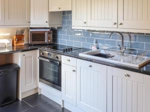 een keuken met witte kasten, een wastafel en een magnetron bij Top Farm Cottage in Oswestry