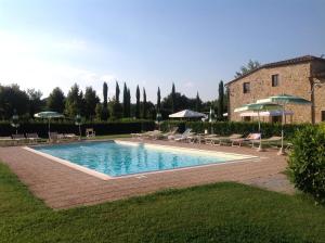 a pool with chairs and umbrellas next to a building at Agriturismo La Peschiera in Casole dʼElsa