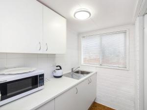 a white kitchen with a sink and a microwave at Comfy Studio with Idyllic Yard in Great Location in Terrigal