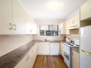 a white kitchen with white cabinets and a sink at Family Beachside Getaway with BBQ and Patio in Terrigal