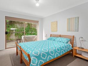 a bedroom with a bed with a blue comforter and a window at Spacious House with Balcony & Pool, Walks to Beach in Terrigal