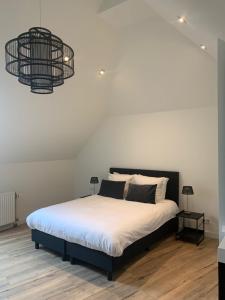 a bedroom with a large bed with white sheets and a chandelier at Verblijf in loft van luxe villa de Vossenberg in Etten-Leur