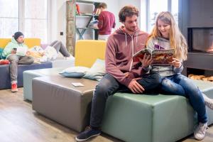 a man and woman sitting on a ottoman in a living room at Oberstdorf Hostel in Oberstdorf