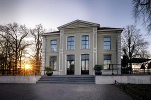 a large white house with the sun setting behind it at Pillows Luxury Boutique Hotel aan de IJssel in Deventer
