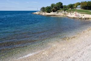 a beach with people sitting on the shore of the water at Hotel Albatros Plava Laguna in Poreč