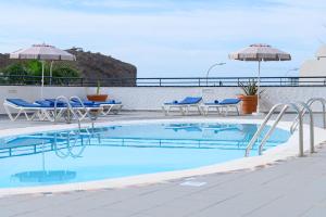 a swimming pool with blue chairs and umbrellas at Marianela Apartment in Puerto Rico de Gran Canaria