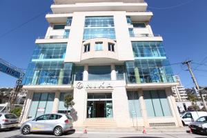 een hoog wit gebouw met auto's geparkeerd voor het bij Nika Hotel in Sarandë