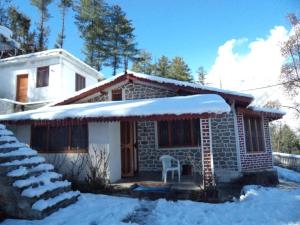 a small stone house with a chair in the snow at Resort With Mesmerizing Mountain Views & Pine Trees in Joshīmath