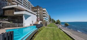 a building with a swimming pool next to the water at Departamento Pucón - Salida directa al Lago Villarrica in Pucón