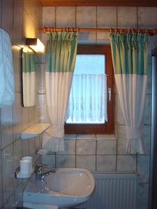 La salle de bains est pourvue d'un lavabo et d'une fenêtre avec des rideaux. dans l'établissement Pension Anneliese, à Schwendt