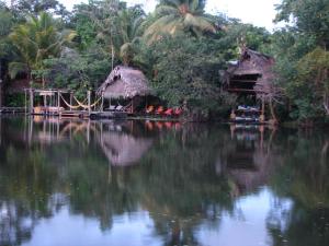 a body of water with two huts and trees at El Hotelito Perdido in Río Dulce
