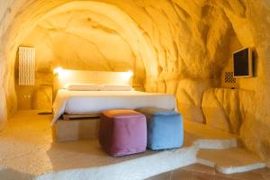um quarto numa caverna com uma cama e dois bancos em La Corte Dei Pastori Luxury em Matera