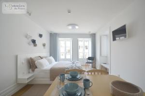 a white room with a bed and a table with cups and dishes on it at A Botoeira da Praça guest house in Viana do Castelo