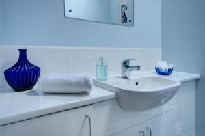 a white bathroom with a sink and a blue vase at Walkers Court By Treetop Property in Cirencester