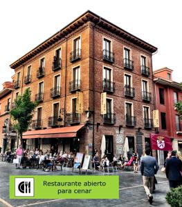 un gran edificio de ladrillo con gente sentada fuera de él en Hotel Spa QH Centro León, en León