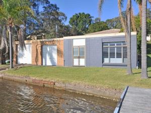 a house by the water with palm trees at The Studio on the Lake at Fishing Point Lake Macquarie in Fishing Point