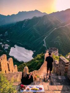 a man and a woman sitting on the edge of a wall looking at a valley at Encounter Garden Great Wall Holiday Guesthouse in Beijing