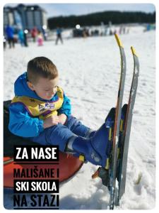 a young boy sitting in the snow next to skis at Lux Apartman Boris in Zlatibor +43 photos