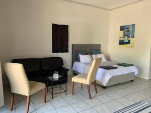 a bedroom with a bed and a couch and chairs at Le Grec Wine Tram Apartment in Franschhoek