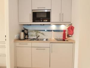una cucina con mobili bianchi, un lavello e un microonde di Ferienwohnung Strandmarie, Haus Loreley, App. 14 a Sankt Peter-Ording