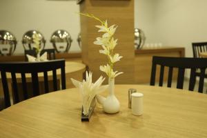 uma mesa de madeira com um vaso branco com flores em VIPs Hotel Olive em Siliguri