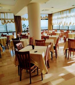 un restaurante con mesas y sillas blancas y ventanas en Hotel Alcazar en Rímini