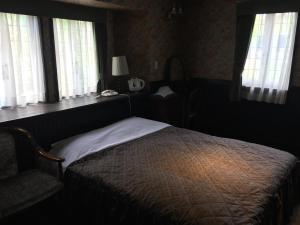 a bedroom with a bed and a chair and windows at Petit Hotel & Restaurant Old Age in Hokuto
