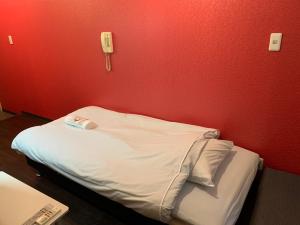 a small bed in a room with a red wall at Exsaison Shirokita 603 in Osaka