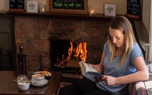 a woman reading a book in front of a fireplace at Dryburgh Arms Pub with Rooms in Melrose