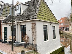 een wit huis met een groen dak naast een kanaal bij Wetterhûske - Huisje aan de gracht in Franeker