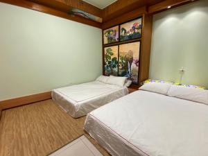 2 Betten in einem Zimmer mit Gemälden an der Wand in der Unterkunft Bridgeside Homestay in Pingtung