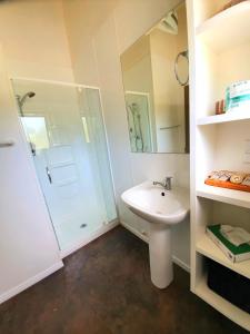 La salle de bains blanche est pourvue d'une douche et d'un lavabo. dans l'établissement Kauri Coast TOP 10 Holiday Park, à Kaihu