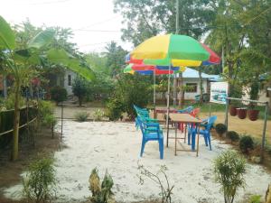 a table and chairs with a colorful umbrella in the sand at Blue Bird Residency in Neil Island