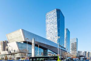 a large glass building in a city with cars at Happy Dragon Universal Vacation Hotel - close to Universal Studio and Wanda Plaza,free shuttle to the Resort,Free Coffee,Laundry in Beijing