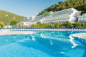duży basen z niebieskimi krzesłami i budynek w obiekcie Hotel Hedera - Maslinica Hotels & Resorts w Rabacu